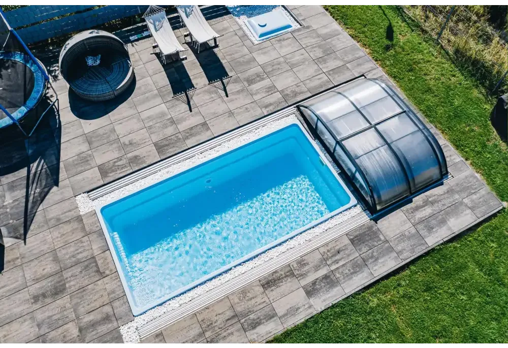 Glasfiberpool Papeete med klart blått vatten och transparent lock på grå stenplattor